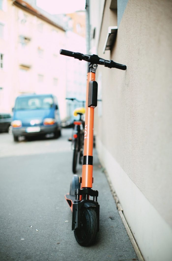 Orange electric scooter leant against a wall.